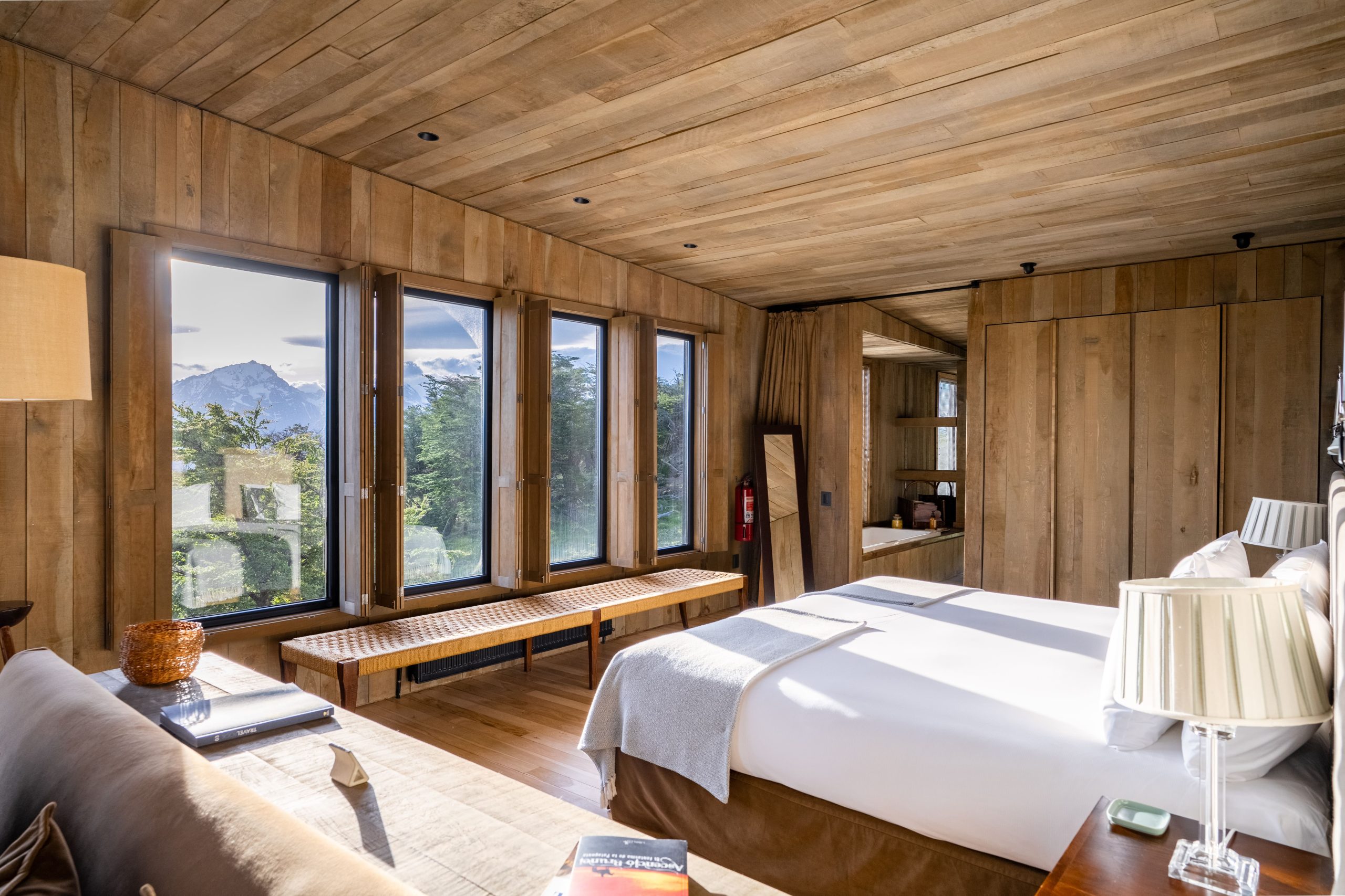 Interior of a private villa at Awasi Patagonia near Torres del Paine National Park, Chile, designed by architect Felipe Assadi with native wood and large windows offering panoramic views of the forest, Lake Sarmiento, and Torres del Paine mountains. The villa features a wood-burning fireplace, central heating, private outdoor hot tub, and includes a private guide and vehicle for personalized excursions.