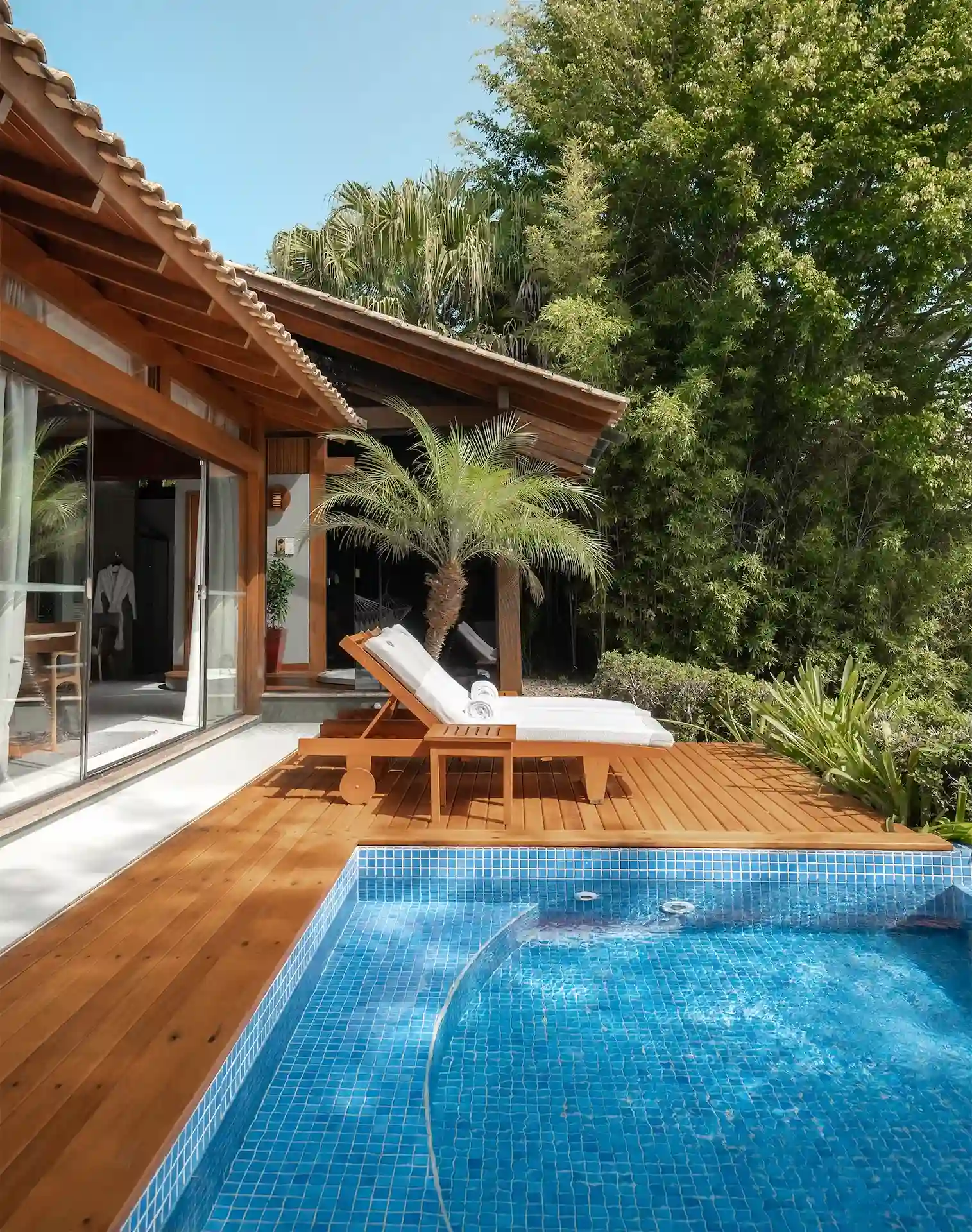 Private villa terrace with wooden deck, lounge chairs, and a small pool surrounded by lush greenery