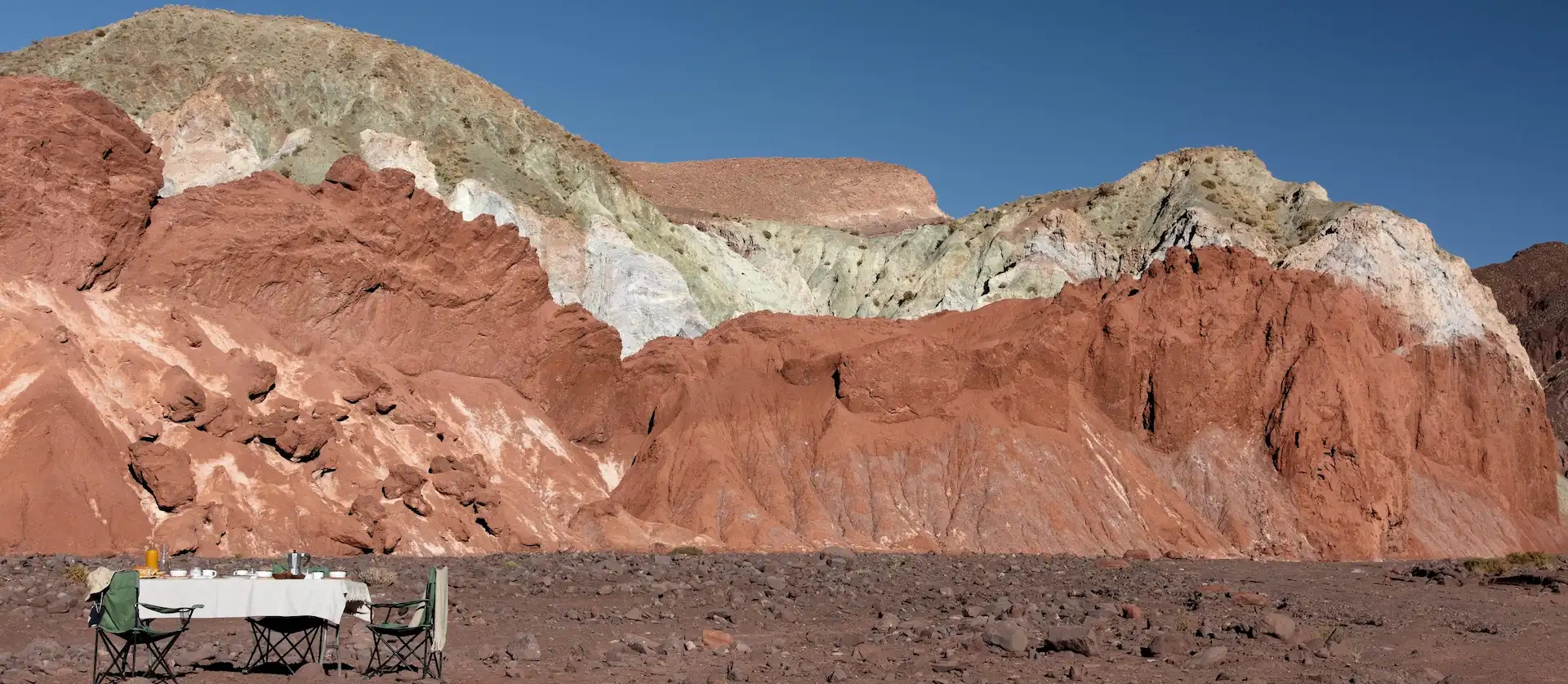 Outdoor dining setup in a desert landscape with colorful rock formations and clear blue sky
